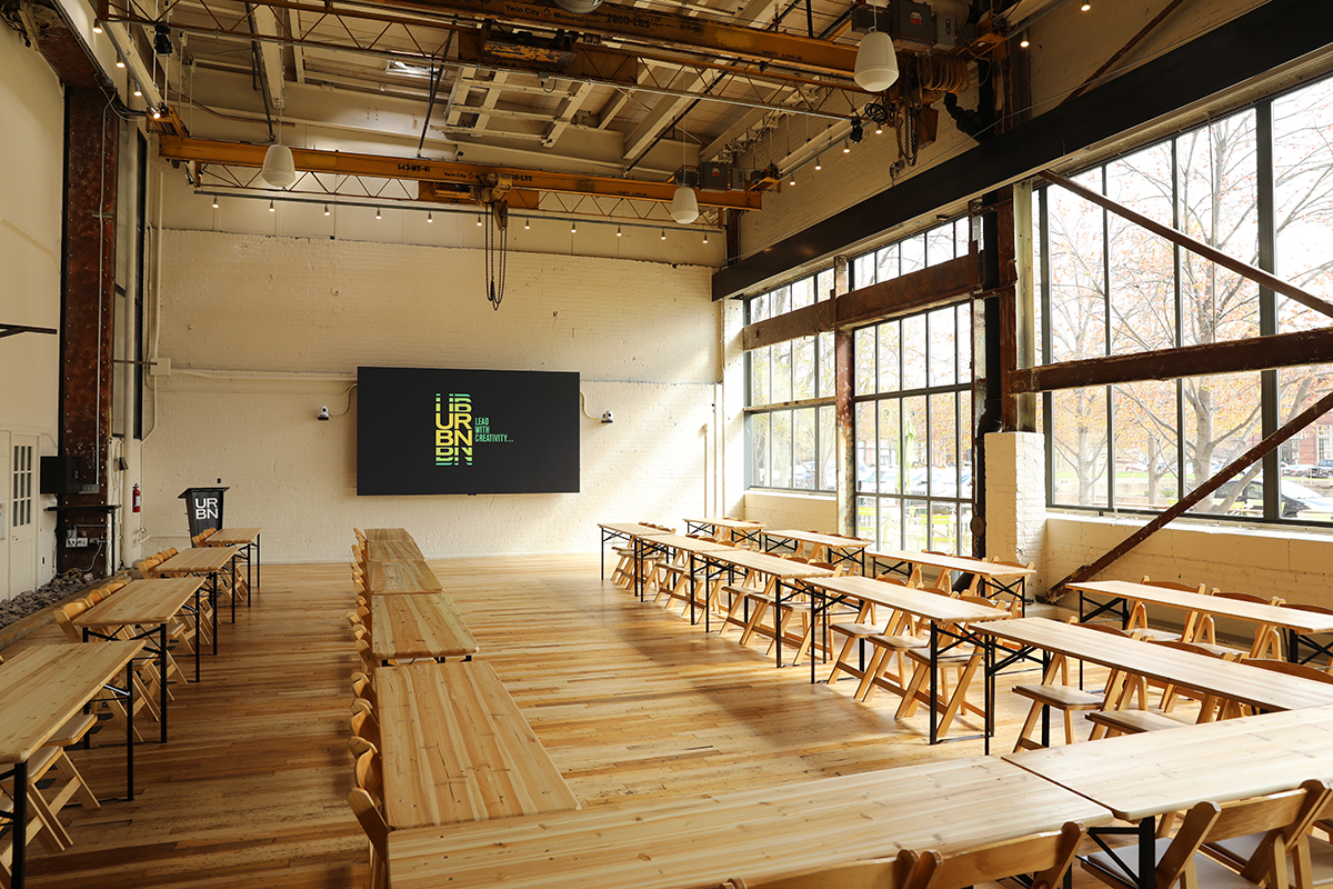 Room with wooden tables and chairs with digital display showing URBN logo